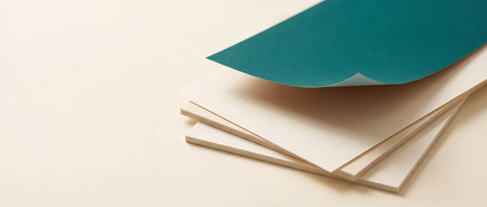 A sheet of teal paper lifting off a stack of cream pages.